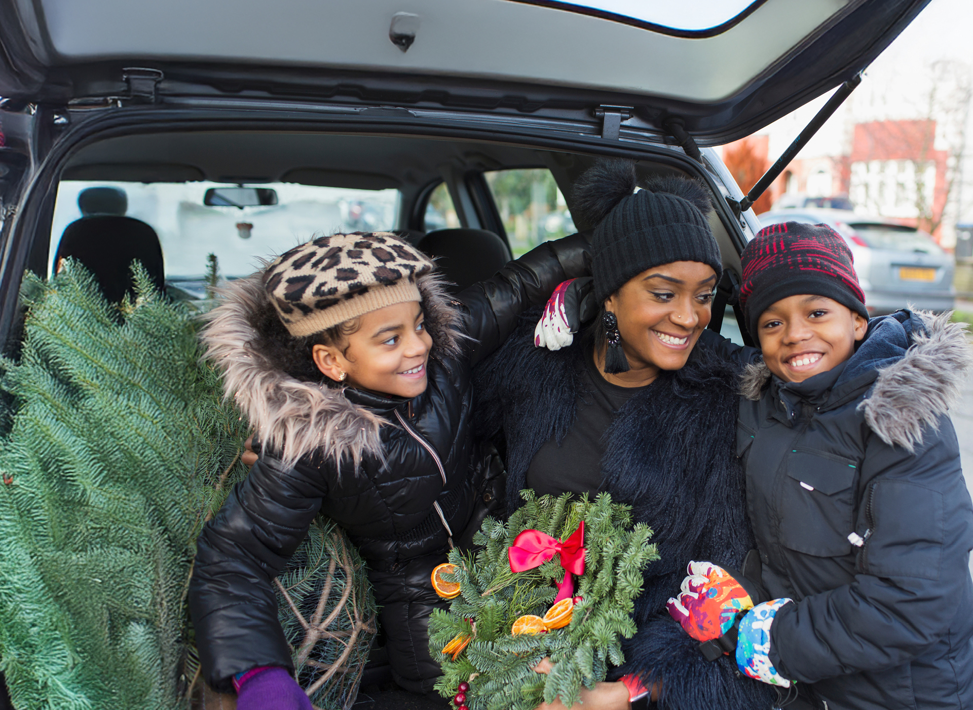 a mom and two kids hold a wreath and get a christmas tree